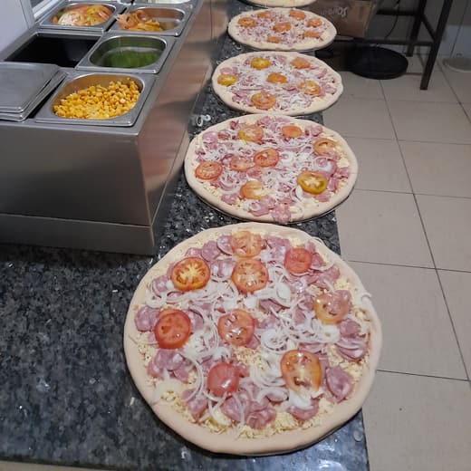 Bancada de montagem com as pizzas enfileiradas antes do forno