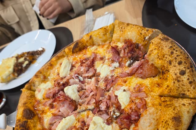 Pizza no centro da mesa com pratos e gente em volta