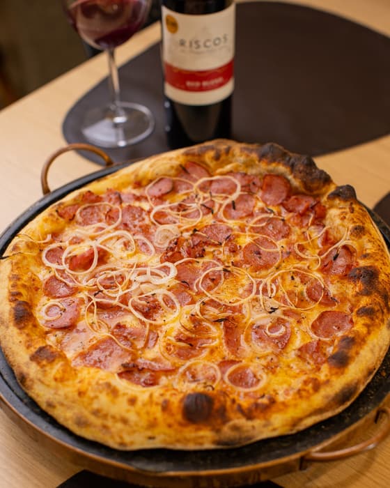 Pizza de calabresa com cebola servida na forma, com vinho ao fundo